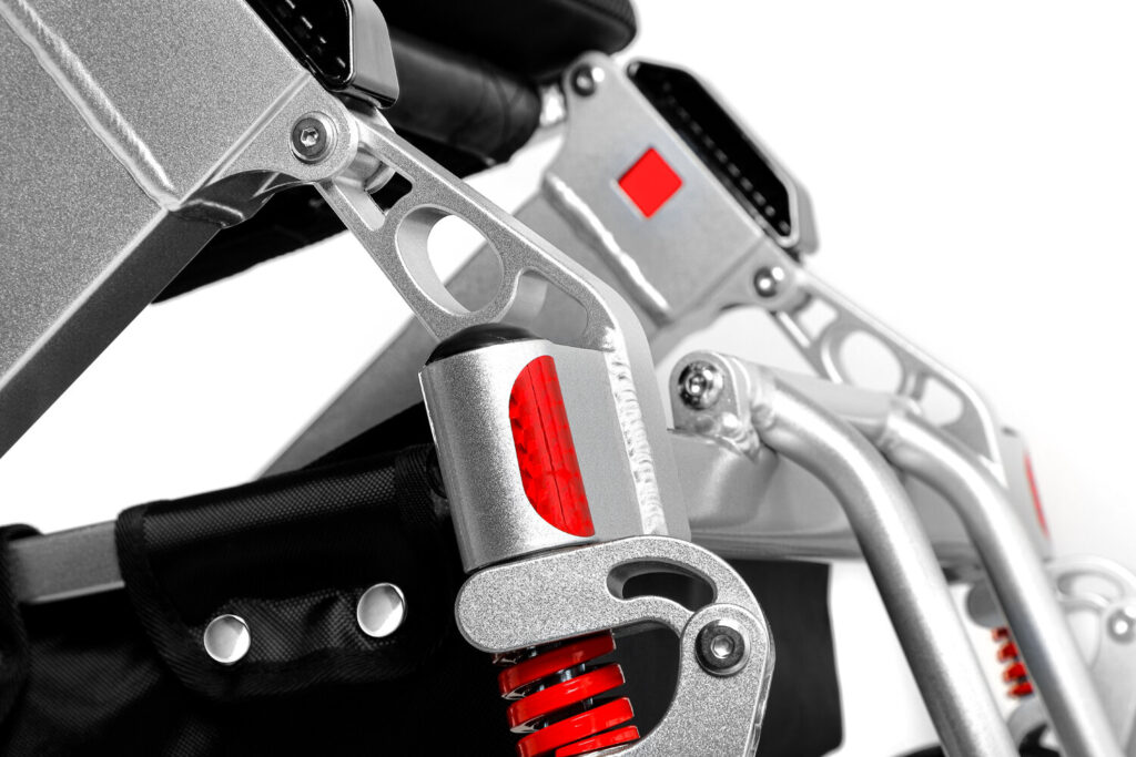 Porto Mobility Ranger Discovery XXL folding power wheelchair, close up of the front frame and red spring caster mount