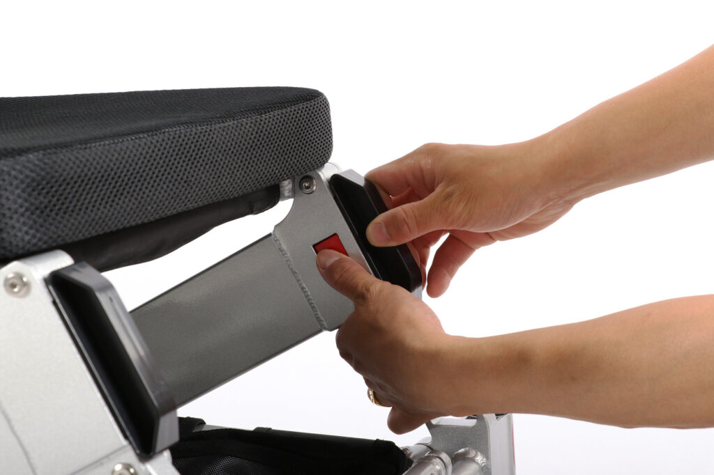 Ranger Maestro reclining folding power wheelchair, two hands at the frame tube end, thumb on the red button